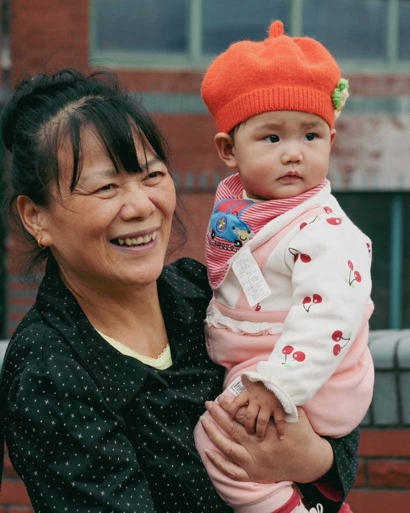 亞洲祖母懷抱戴橘色帽子的嬰兒，象徵祖孫之間的唯一一張合照