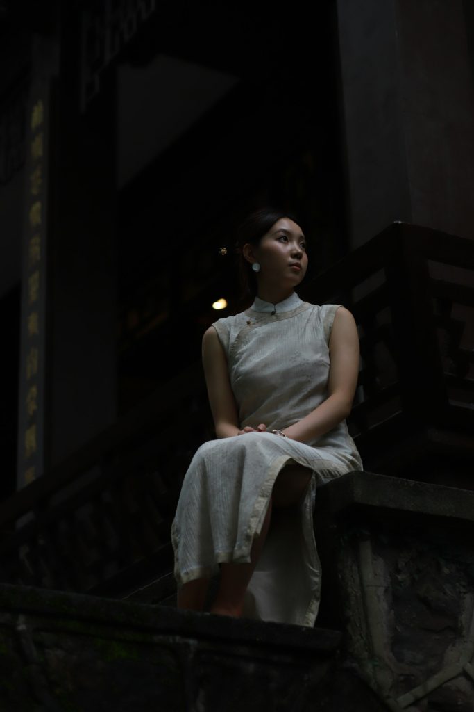 東方女性身穿中式傳統服飾坐於老石階上,象徵阿嬤年輕時穿旗袍的容顏