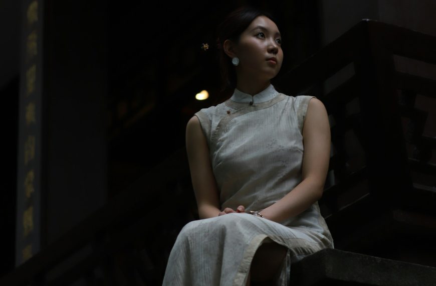 東方女性身穿中式傳統服飾坐於老石階上,象徵阿嬤年輕時穿旗袍的容顏