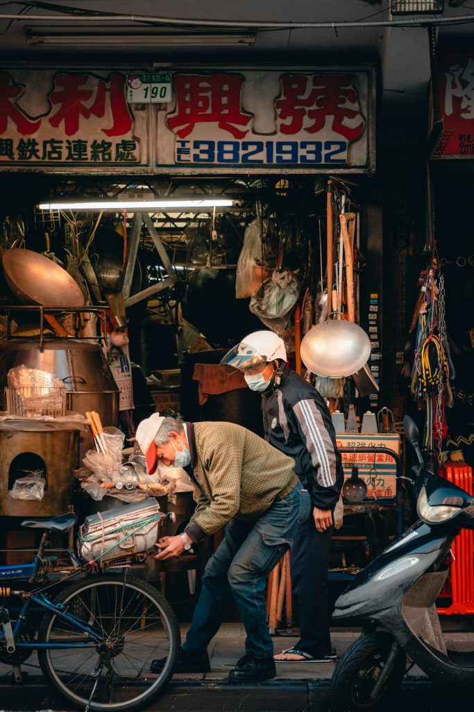 台灣傳統市場的鐵店招牌與兩位戴口罩工作的東方男性,象徵阿公賣魚五十年的攤位